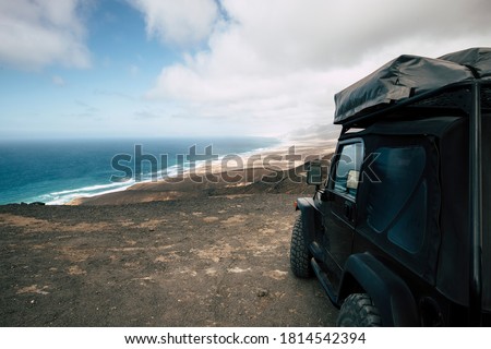 Black off road car parked on the top of a valley with amazing view on a wild beach with nobody - off grid roof tent and adventure lifestyle travel concept