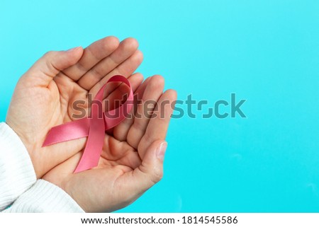 Female hands hold pink ribbon on blue background top view