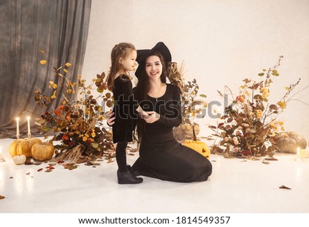 Happy mother and daughter wearing spooky black costumes of witches in studio with Halloween decorations