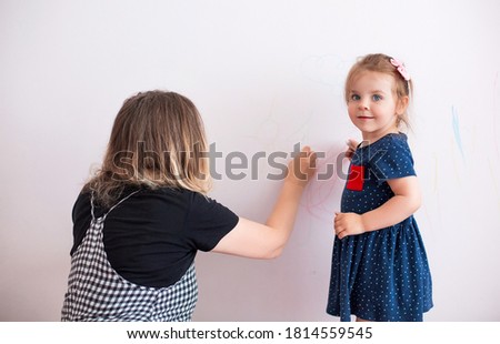 Side view of woman scolding little girl for painting walls in modern apartment