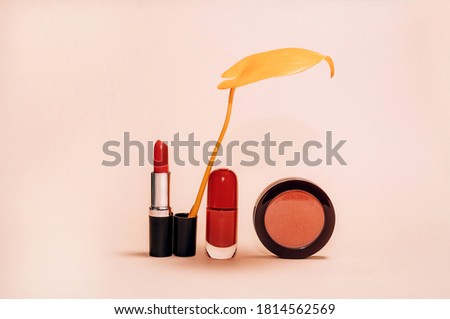 Decorative composition with cosmetics, woman beauty products, red lipstick, blush and nail polish, decorated with autumn yellow leaf on light background, fashion still-life