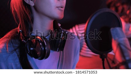 Young asian woman singing while man in background playing acoustic guitar. Young contemporary sound operator handsome male processing music. recording studio mixing song band concept.