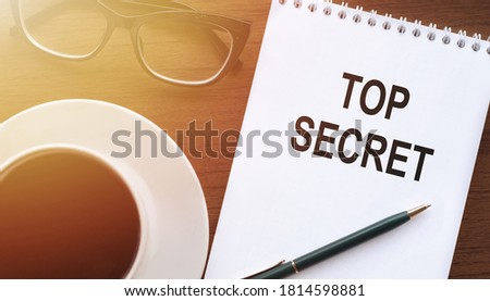 Concept of Top Secret, text Top Secret on notebook with cup of tea and glasses
