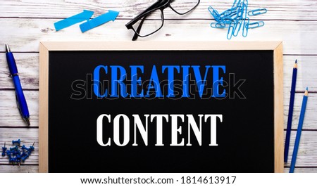 CREATIVE CONTENT written on a black note-board next to blue paper clips, pencils and a pen. Creative concept