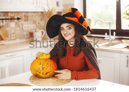 Happy and beautiful girl in the kitchen at home in a suit and make-up with a pumpkin lantern smiling