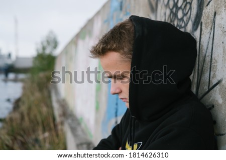 portrait of a sad lonely teenager / young guy in a black hoodie in an abandoned place near the port Royalty-Free Stock Photo #1814626310