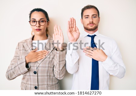 Beautiful couple wearing business clothes swearing with hand on chest and open palm, making a loyalty promise oath  Royalty-Free Stock Photo #1814627270