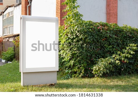 Vertical billboard on a green lawn near a brick wall, mock up.