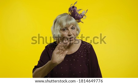 Don't do it. Senior old woman warning of mistake, showing admonishing finger gesture, disapproval sign, asking to be careful. Elderly stylish lady grandma on yellow background in studio