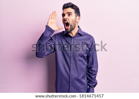 Young handsome man with beard wearing casual shirt shouting and screaming loud to side with hand on mouth. communication concept. 