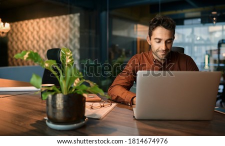 Business working on a laptop and going over paperwork while sitting at his desk in a quiet office after hours Royalty-Free Stock Photo #1814674976