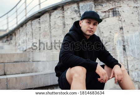 City portrait of handsome guy wearing black blank hoodie or sweatshirt and baseball cap  