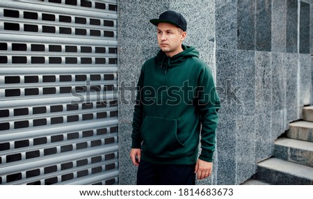 City portrait of handsome guy wearing green (watercolor) blank hoodie or sweatshirt and black baseball cap 