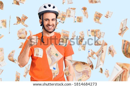 Young handsome man wearing bike helmet smiling happy and positive, thumb up doing excellent and approval sign