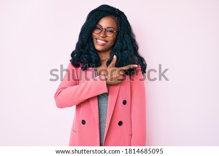 Beautiful african woman wearing business jacket and glasses cheerful with a smile of face pointing with hand and finger up to the side with happy and natural expression on face 