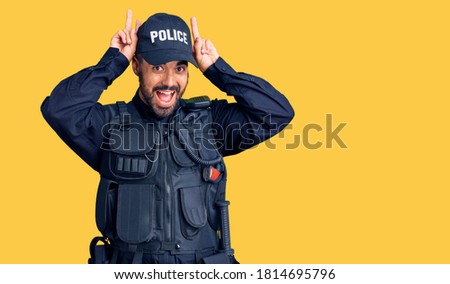 Young hispanic man wearing police uniform posing funny and crazy with fingers on head as bunny ears, smiling cheerful 