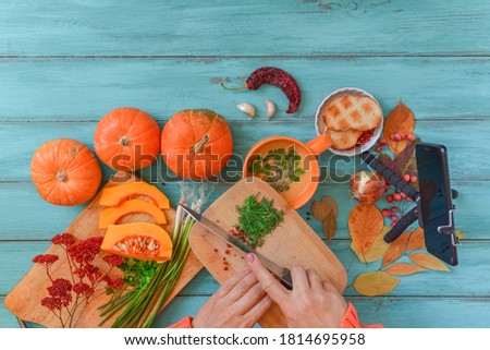 Pumpkin soup on blue wooden table, vintage. Woman hands, cooking process. Food blogger recording video with mobile phone on tripod, holding remote shutter. Thanksgiving, vegan. Flat lay, top view.