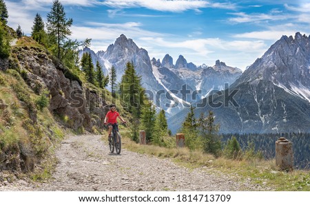 nice and active senior woman riding her electric mountain bike on a old military road from Toblach upt to the summit of Marchkinkele with spectacular view to the Three peaks of Lavaredo, South Tirol, 