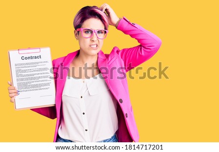 Young beautiful woman with pink hair holding clipboard with contract document confuse and wondering about question. uncertain with doubt, thinking with hand on head. pensive concept. 