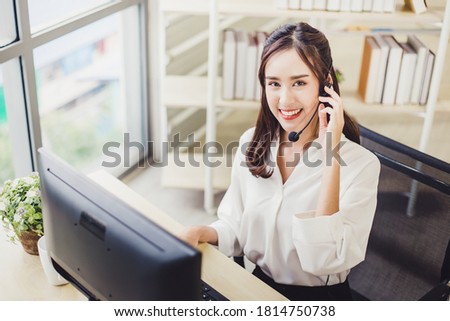 Beautiful Asian woman customer service talking on headset and looking at the camera in call center. Young businesswoman or operator working on support online at modern office.