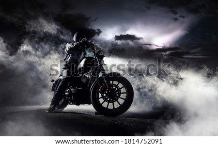 Detail of high power motorcycle chopper with man rider at night. Fog with backlights and dramatic sky on background. Royalty-Free Stock Photo #1814752091