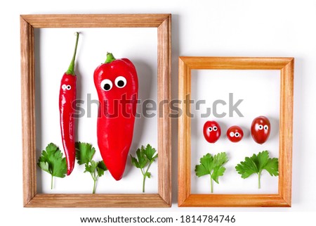 Red peppers and cherry tomatoes with googly eyes inside the wooden picture frame. Creative vegetable composition. Funny food