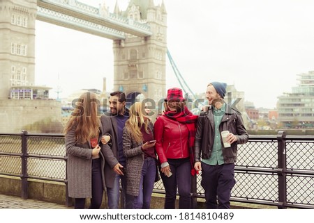 Group of happy young friends having fun on city street. Group of millennial people walking through city park together, near of  bridge. Travel and friendship concept.