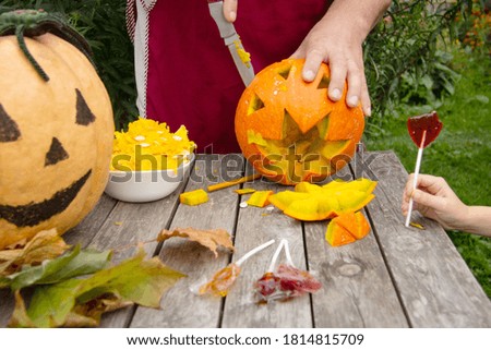 Mezhina cuts out a pumpkin lantern for halloween. On the street on a wooden table is another pumpkin and sweets.