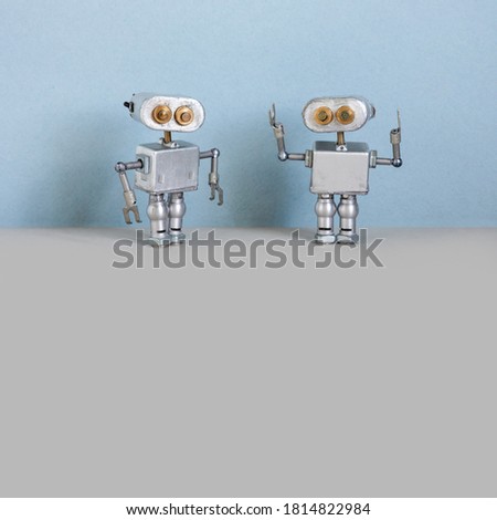 Robots communication. Two simplified metal silver robotics toys on light blue wall, gray floor background. Copy space