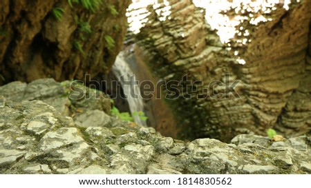 mossy stone relief boulder on a blurred background of a thin stream of waterfall surrounded by textured cave walls