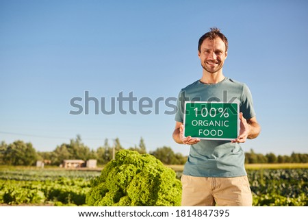 Portrait of smiling man holding ORGANIC FOOD sign and looking at camera while standing at vegetable plantation outdoors in sunlight, copy space
