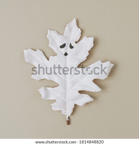 Flat lay Halloween background made with autumn leaf painted in white like ghosts. Minimal season holiday concept