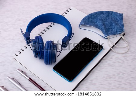 study kit or podcast in covid 19 or quarantine. blue notebook, pens, earphones or earphones cell phone and face mask on textured background