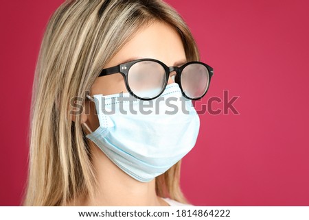 Woman with foggy glasses caused by wearing disposable mask on pink background. Protective measure during coronavirus pandemic Royalty-Free Stock Photo #1814864222