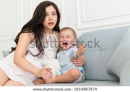 sad baby crying near woman - tantrum child with mother on the sofa 