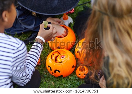 High angle view at group of kids wearing costumes taking candy from Halloween buckets outdoors, copy space