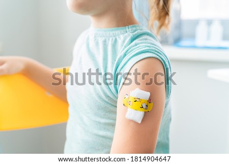 Vaccination of little girl in doctor's office.Kids funny adhesive plaster,gauze napkin.Sits on chair.Vaccine for covid-19 coronavirus,flu,infectious diseases.Injection.Clinical trials for human,child. Royalty-Free Stock Photo #1814904647
