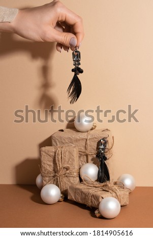 Girl's hand with earring with a feather is over the paper gifts and white christmas balls isolated on beige background. Holiday concept