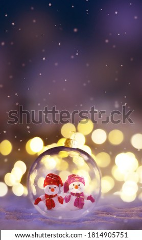 Christmas glass transparent ball with a snowmen inside on snow. Christmas lights glitter background.