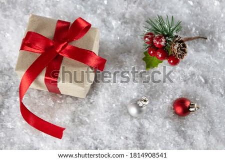 Christmas gift box with a red bow on the snow. Christmas tree toy and spruce branch with red berries. View from above. Copyspace