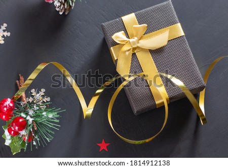 Christmas gift box with a gold bow on a black background. Spruce branch with red berries. Copyspace