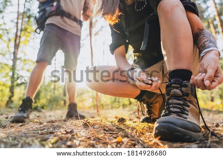 Close up of young female hiker tying shoelaces and getting ready for trekking in forest with man on background. Royalty-Free Stock Photo #1814928680