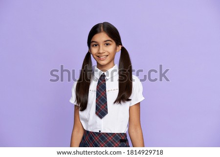 Smiling smart indian hispanic preteen girl with ponytails wearing school uniform standing isolated on lilac violet background. Happy latin kid, schoolgirl primary student looking at camera, portrait.