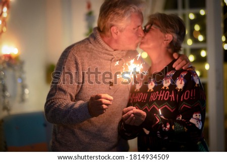 Defocused senior couple kissing celebrating Christmas event with sparks. Lights and Christmas tree in the background - active retired elderly people in love