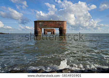 frontal view of the ruins of the former jetty in Eckwarderhörne (district Wesermarsch, Germany) under vivid blue sky with scenic white clouds during high tide