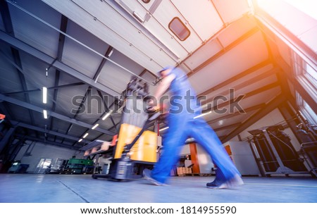 A worker in a warehouse uses a hand pallet stacker to transport pallets. Royalty-Free Stock Photo #1814955590