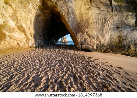 Tourists footprints lead to cove entrance at sunrise, Cathedral Cove  with Te Hoho rock and blue water and sky on Coromandel Peninsula New Zealand.