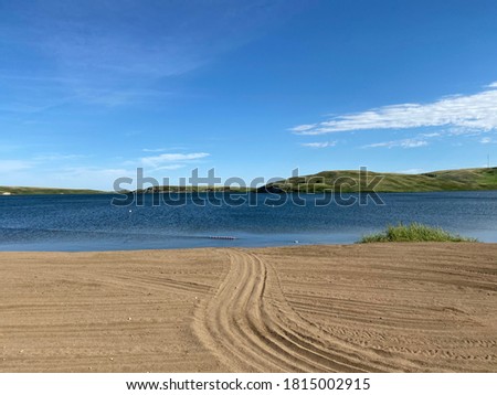 Tire tracks in sand disappearing into a blue lake under a clear sky