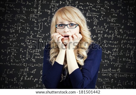 Closeup portrait nervous, stressed woman, nerdy scared student with eyeglasses biting fingernails looking anxiously, afraid of finals, isolated chalkboard background filled with math, physics formulas