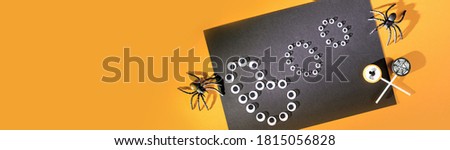 Happy Halloween boo of pop eyes with spiders and nets on orange background and festive lollypops candies. Flat lay with copy space